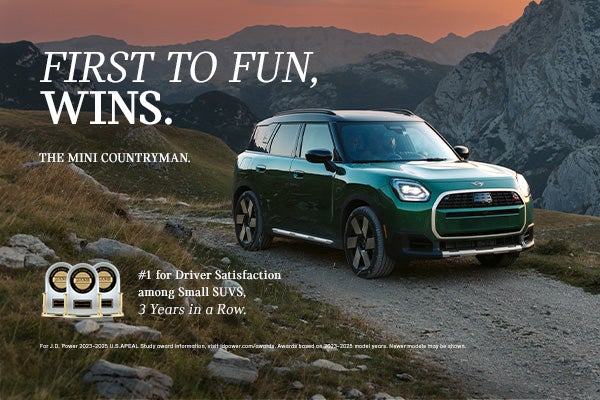 Front passenger side view of a green MINI Countryman driving on a mountainous road.