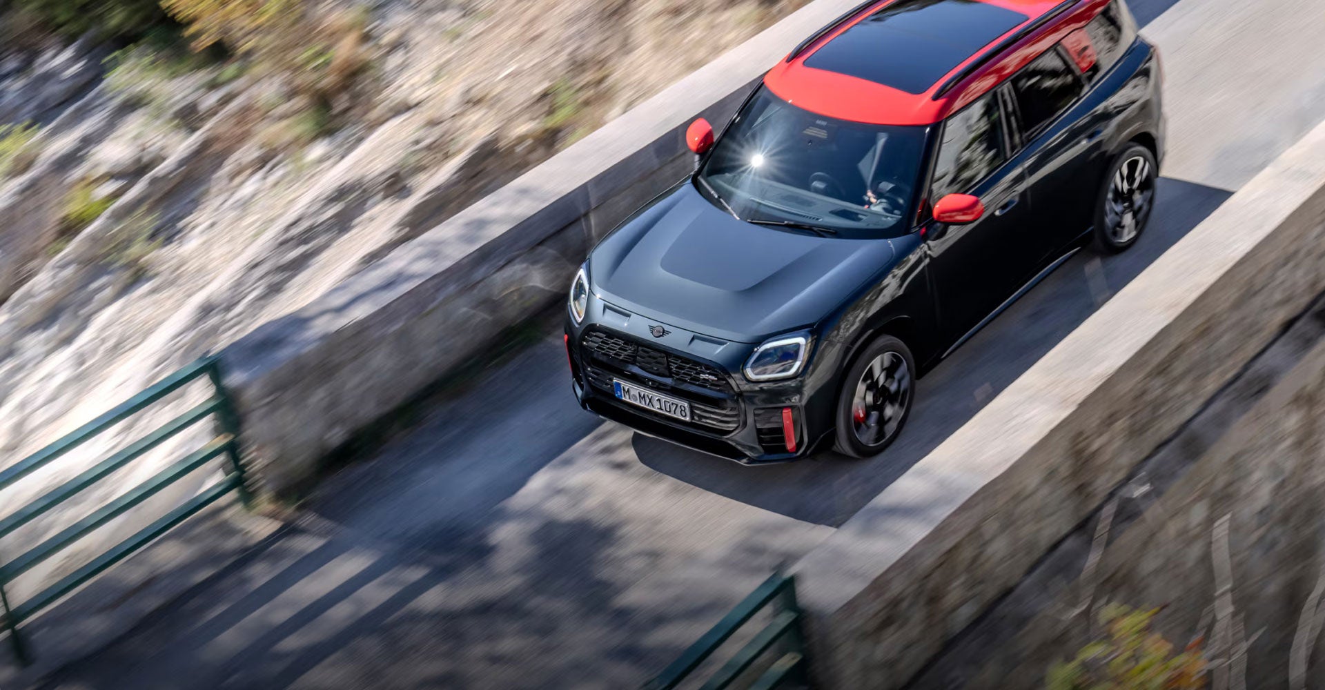 Birds-eye view of the MINI JCW Countryman ALL4 driving over a cement bridge with rock beneath it. 